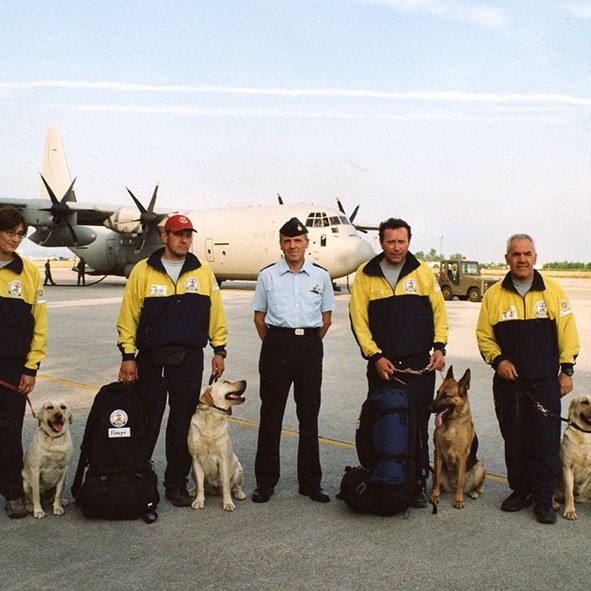 Un gruppo di uomini e cani in piedi davanti a un aereo.