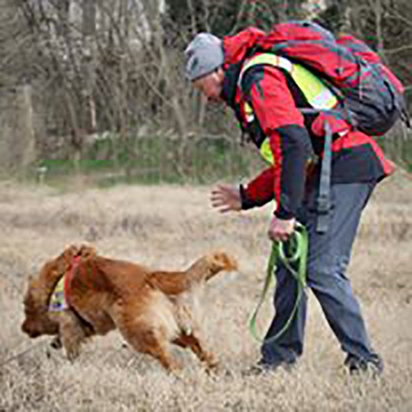Un uomo con uno zaino porta a spasso un cane in un campo.
