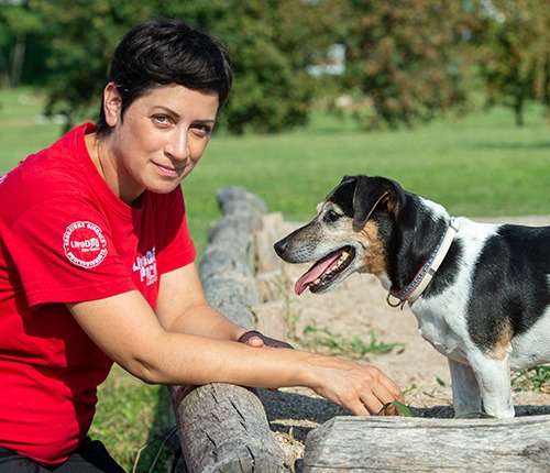 Una donna accarezza un cane con una maglietta rossa.
