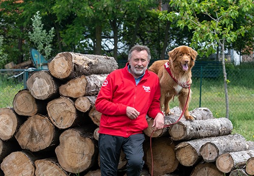 Un uomo e il suo cane in piedi accanto a una pila di tronchi.