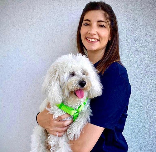 Una donna che tiene in braccio un cane bianco davanti a un muro.