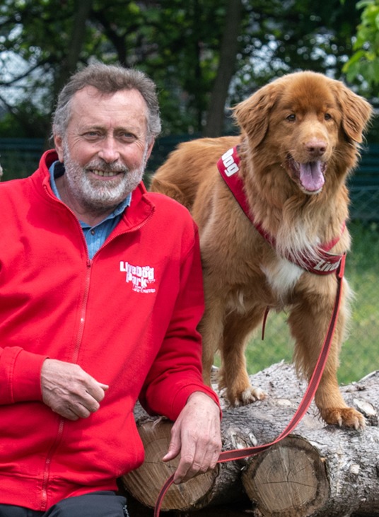 Un uomo con una giacca rossa con un cane su un tronco.