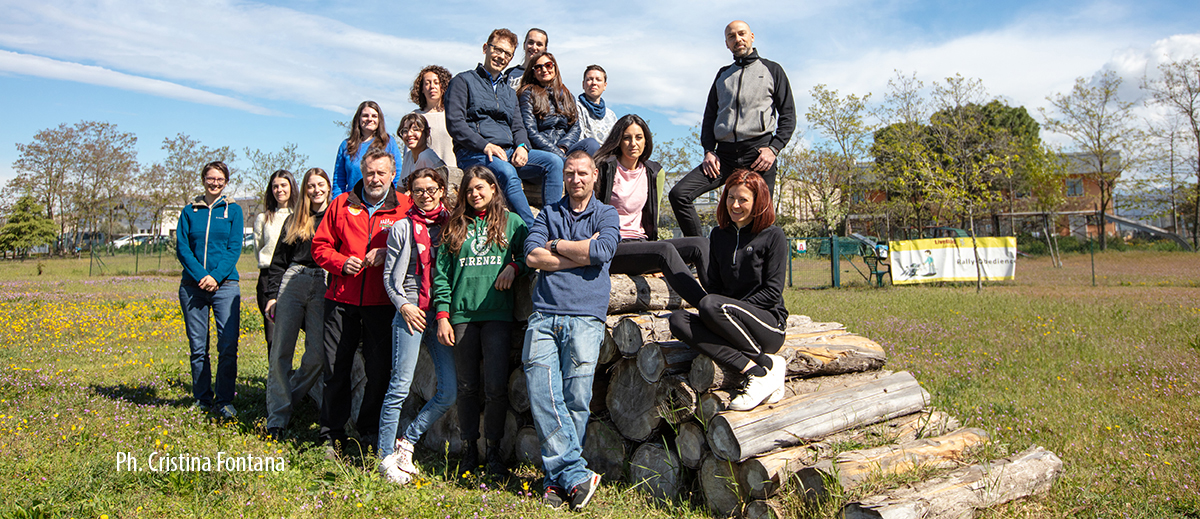 Un gruppo di persone in posa davanti ad una catasta di tronchi.