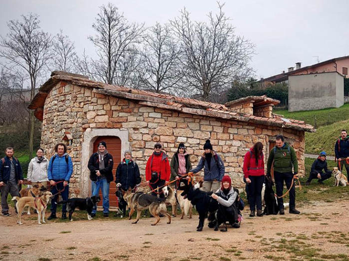 Un gruppo di persone che passeggia con i cani davanti ad una casa in pietra.